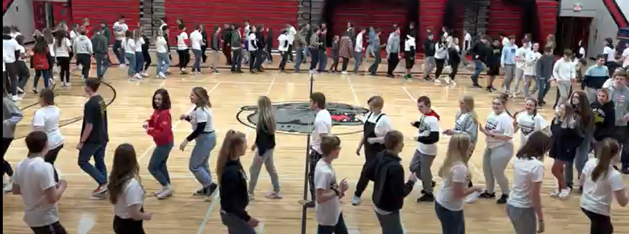 Student/staff in a circle moving around in the gym dancing a Fjaskern